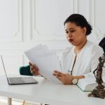 Une avocate noire lisant des documents juridiques à son bureau dans un bureau moderne.